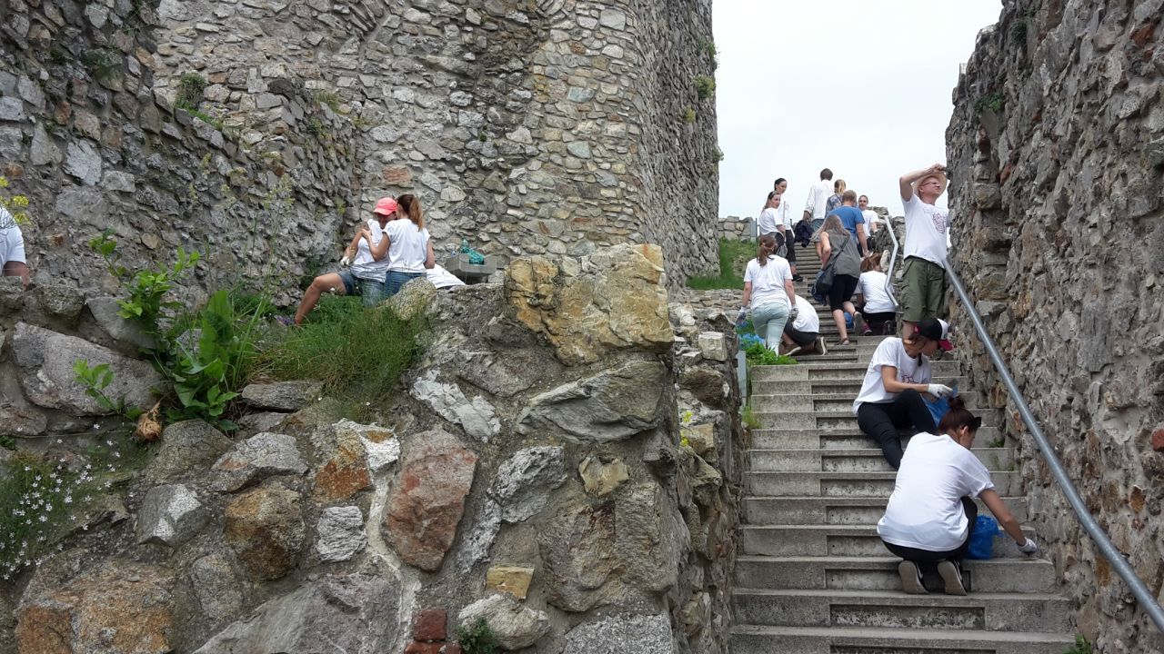 na pravo ľudia čistia schody vedľa starých kamenných hradieb, na ľavo dvaja ľudia čistia menšiu hradbovú terasu