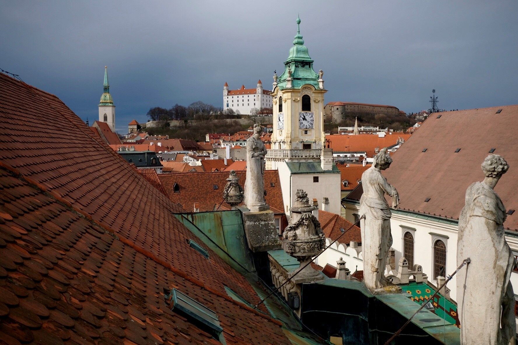 záber na panorámu mesta z pozície strešných sôch primácialného paláca, v pozadí je vidieť vežu starej radnice, bratislavský hrad a vežu dóm sv. Martina